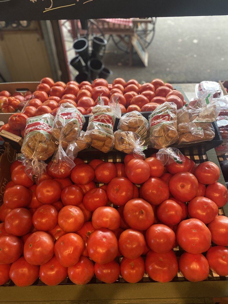 Fresh red tomatoes stacked neatly in a market display, accompanied by packaged baked goods in transparent bags. The vibrant colors and organized arrangement highlight the freshness of the produce.